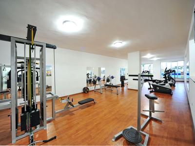 Una palestra spaziosa con pavimento in legno e varie attrezzature per l'esercizio sotto luci a soffitto luminose.