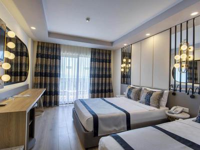 Moderní hotelový pokoj se dvěma postelemi queen, televizí a velkým oknem se závěsy.