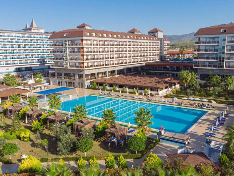 Velký hotel s několika budovami a velkým bazénem obklopeným palmami pod jasnou oblohou.