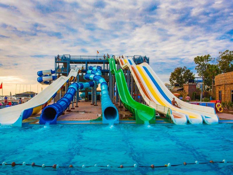 Vícebarevné vodní skluzavky nad modrým bazénem ve vodním parku při západu slunce