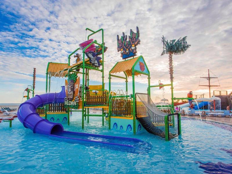 Barevná vodní herní konstrukce se skluzavkami v venkovním bazénu při západu slunce.