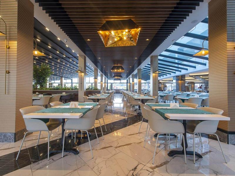 Moderní světlá restaurace s mramorovou podlahou, stoly a židlemi v elegantním prostředí.