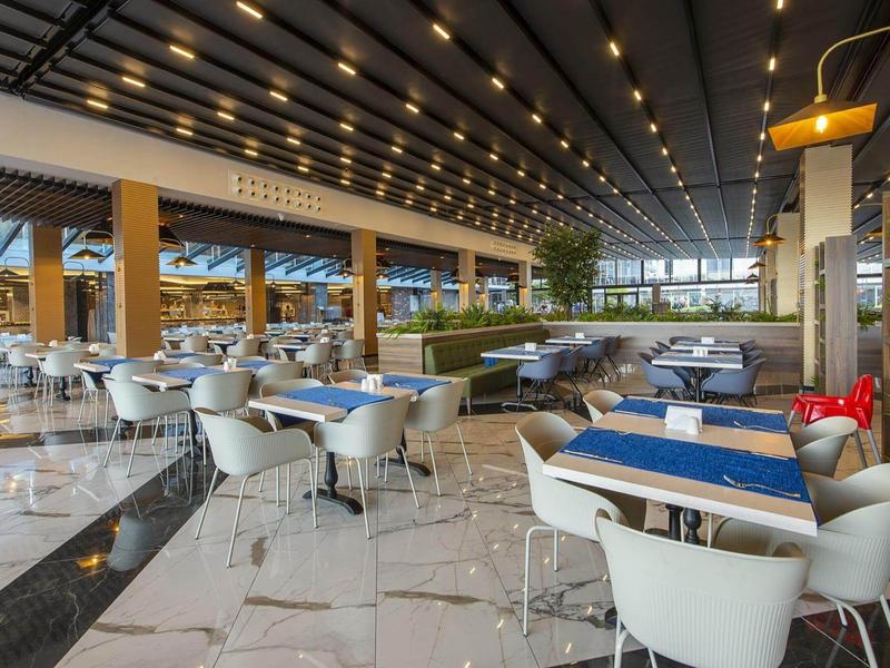 Moderní, světlá hotelová restaurace s bílými židlemi a modrými ubrusy.