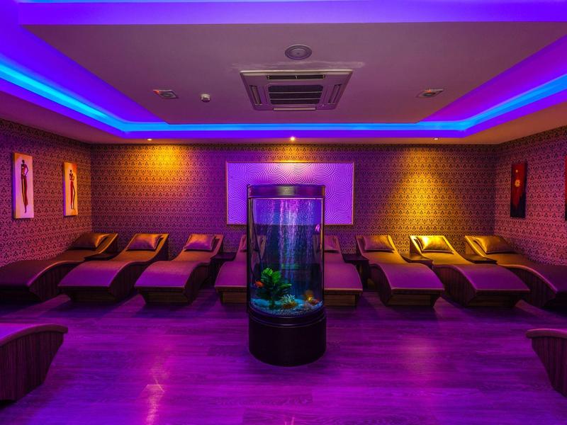 Prostor pro relaxaci s lehátky, ambientním osvětlením a dekorativním akváriem uprostřed.