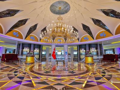 Gran vestíbulo de hotel con araña, suelo decorativo y banderas en el centro.