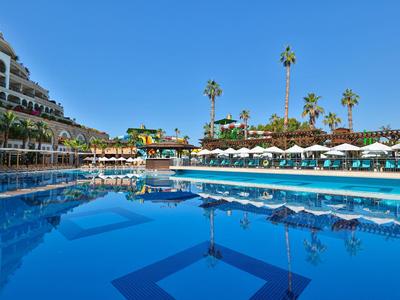 Gran piscina del hotel con tumbonas, sombrillas y palmeras bajo un cielo despejado.