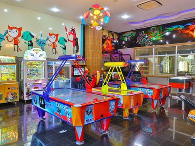 Sala de juegos colorida con mesas de air hockey, máquinas de garra y murales animados.
