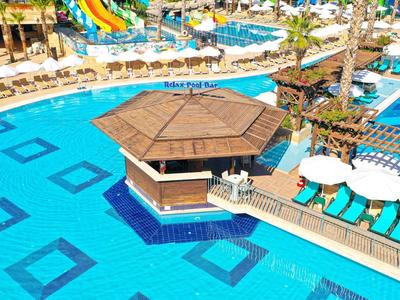 Gran piscina con suelo de azulejos azules y caseta central, rodeada de tumbonas.