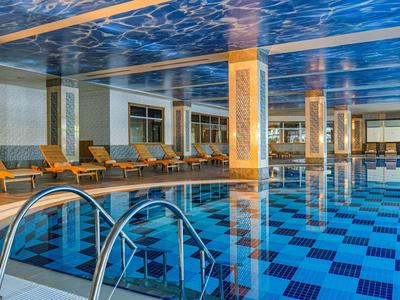 Piscina cubierta con agua azul, escalera de piscina y cómodas tumbonas en las paredes.