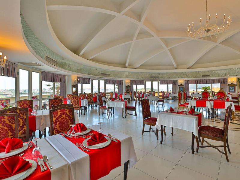 Restaurante elegante con mesas blancas, sillas rojas, gran cúpula y vista al mar.