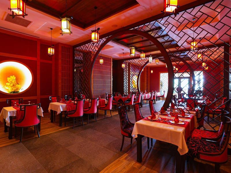 Restaurante elegante con iluminación roja y detalles de madera, mesas con manteles blancos y rojos.