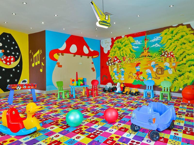 Sala de juegos colorida con murales grandes, juguetes blandos y alfombra multicolor en un área del hotel.