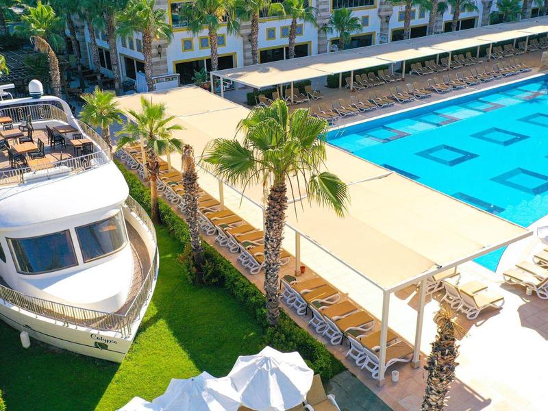 Área moderna de piscina con tumbonas, palmeras y un gran modelo de barco junto a la piscina.