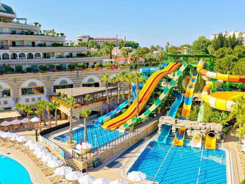 Toboganes de agua y piscinas en un resort hotelero soleado con tumbonas y entorno verde.