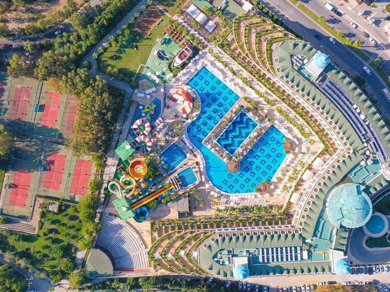 Vista aérea de un complejo hotelero con varias piscinas y canchas de tenis cerca de áreas verdes.