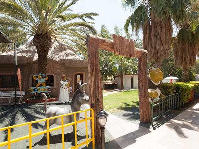 Słoneczny teren zewnętrzny hotelu z palmami, miejscami do siedzenia i drewnianą bramą.