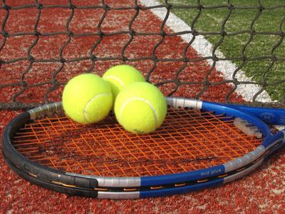 Drei gelbe Tennisbälle liegen auf einem Tennisschläger auf dem roten Tennisplatzboden.