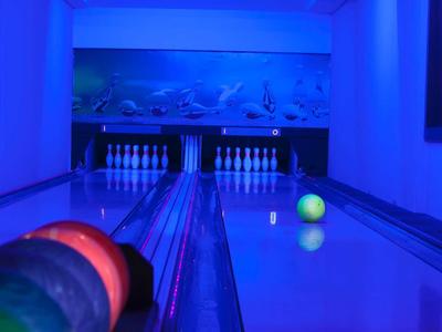 Blick auf eine Bowlingbahn mit leuchtenden Kugeln und Pins unter blauem Licht.