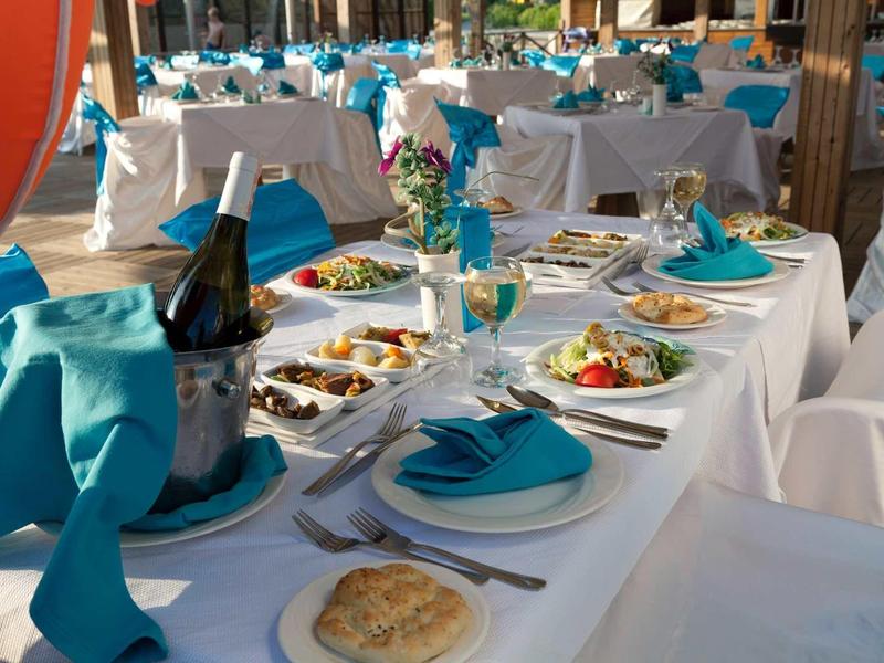 Elegancko nakryty stół z białymi pokrowcami i niebieskimi serwetkami w sali eventowej.