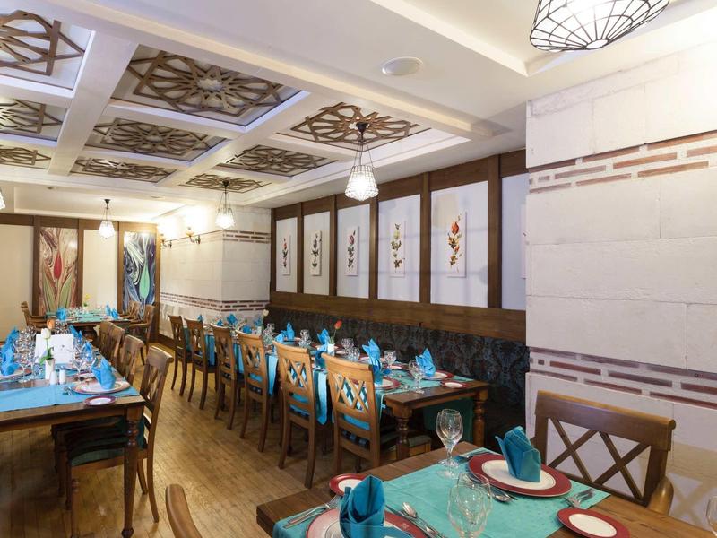 Elegancka jadalnia z niebiesko nakrytymi stołami i ozdobnymi panelami sufitowymi.