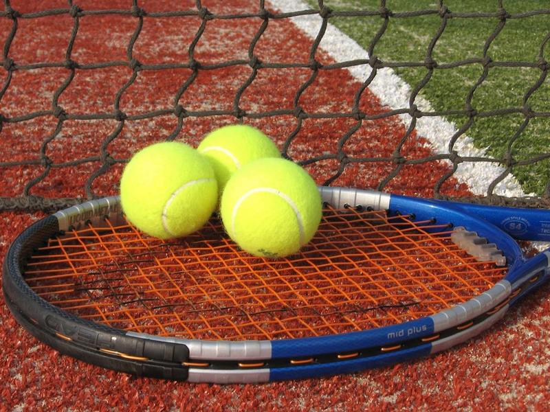 Trzy żółte piłki tenisowe leżą na rakiecie na korcie.