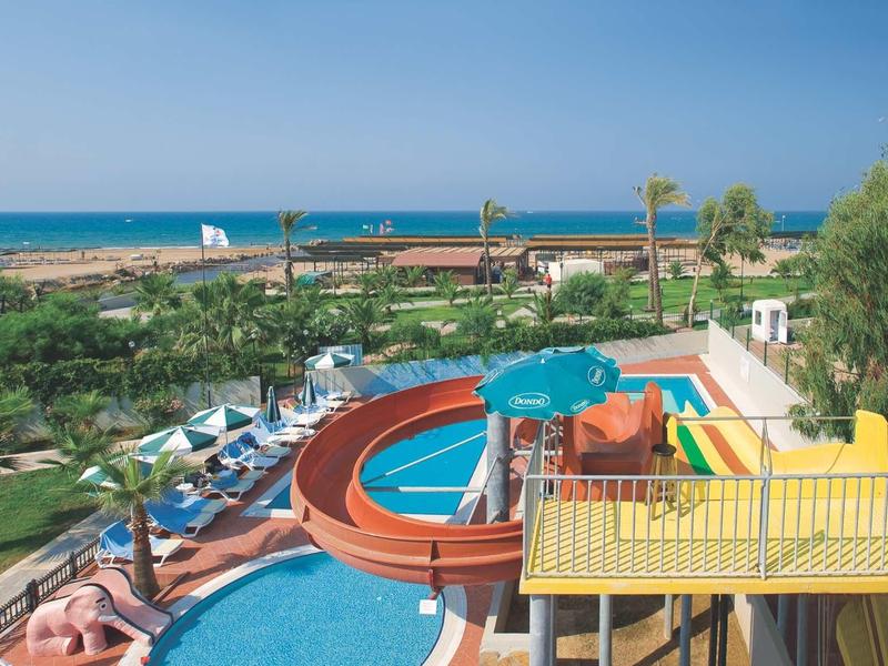 Park wodny z zjeżdżalniami, basenem, leżakami, palmami i widokiem na morze w słoneczny dzień