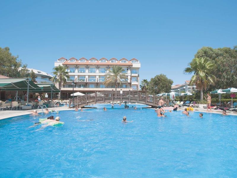 Duży basen na świeżym powietrzu z palmami i budynkiem hotelu w tle pod bezchmurnym niebem.