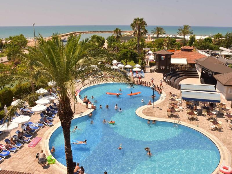 Duży basen na zewnątrz z leżakami i palmami, w tle widok na morze