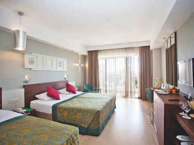 Helles Hotelzimmer mit zwei Betten, roten Kissen, Balkon und moderner Einrichtung.