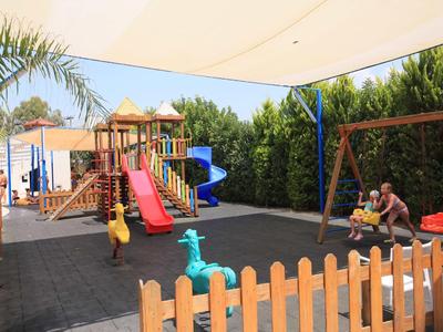 Spielplatz mit Rutsche, Schaukel, Sandkasten und Klettergerüst unter Sonnensegel im Freien.