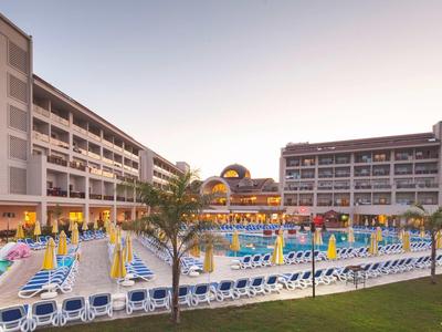 Großes Hotel mit Pool, vielen Liegestühlen, bunten Sonnenschirmen und Palmen bei Sonnenuntergang.