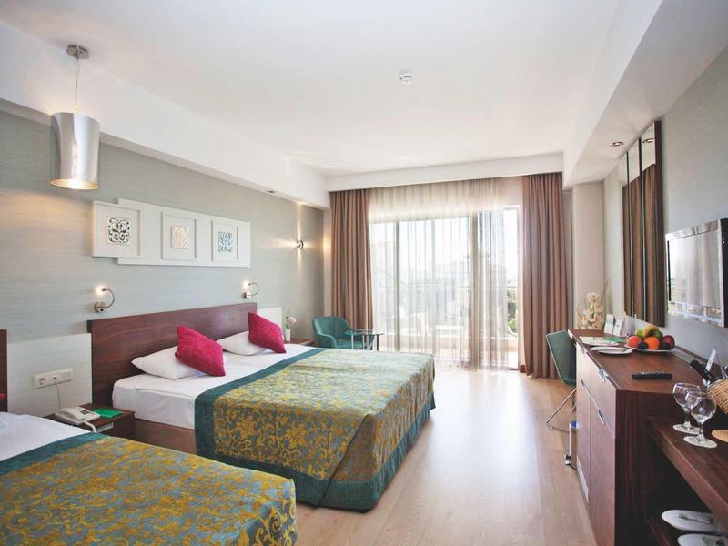 Bright hotel room with two double beds, TV, balcony, and modern decor.