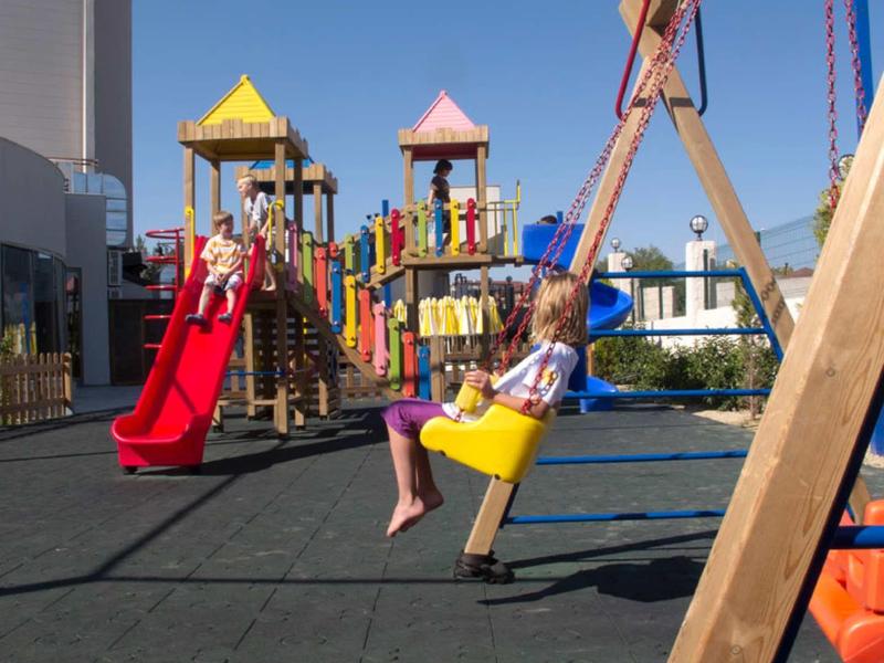 Children playing on a colorful playground with slides and swings on a clear day.