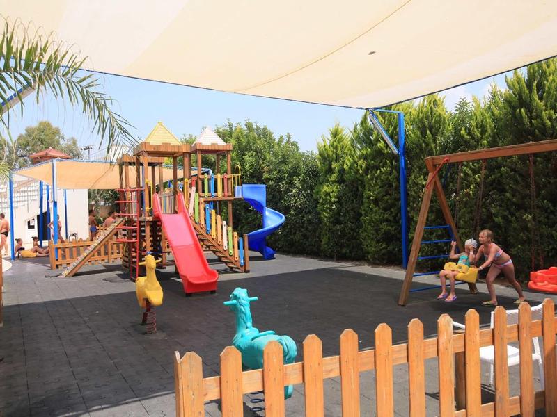 Playground with slide, swing, and climbing frame next to a hedge in sunny weather