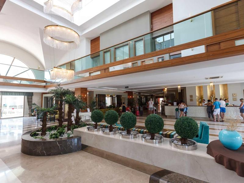 Hotel lobby with round green plants, fountain, and modern seating areas under bright lighting.