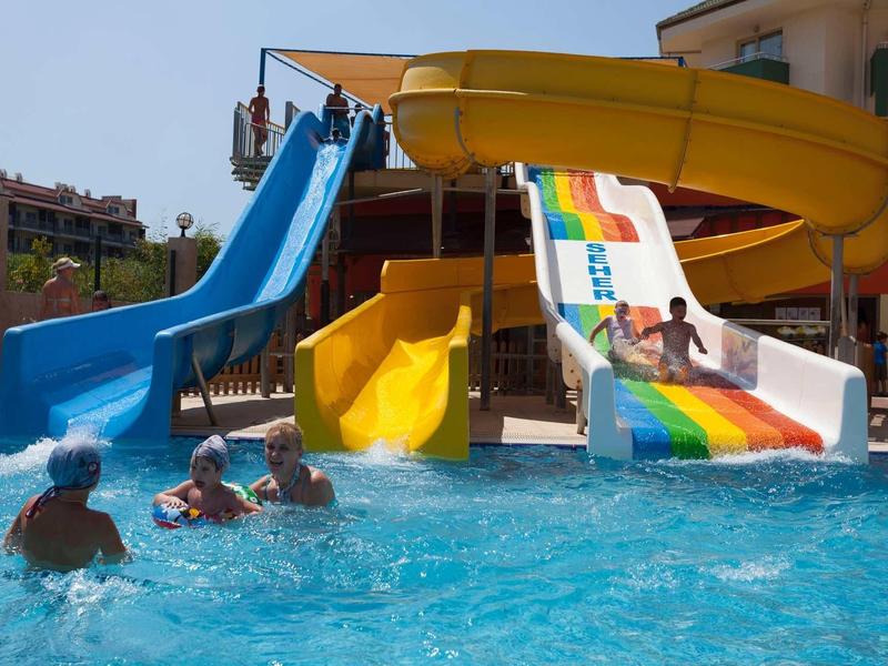 Children sliding down colorful water slides in a pool with adults in the water.