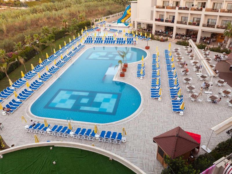 Large hotel pool with blue lounge chairs and umbrellas beside a modern hotel building.