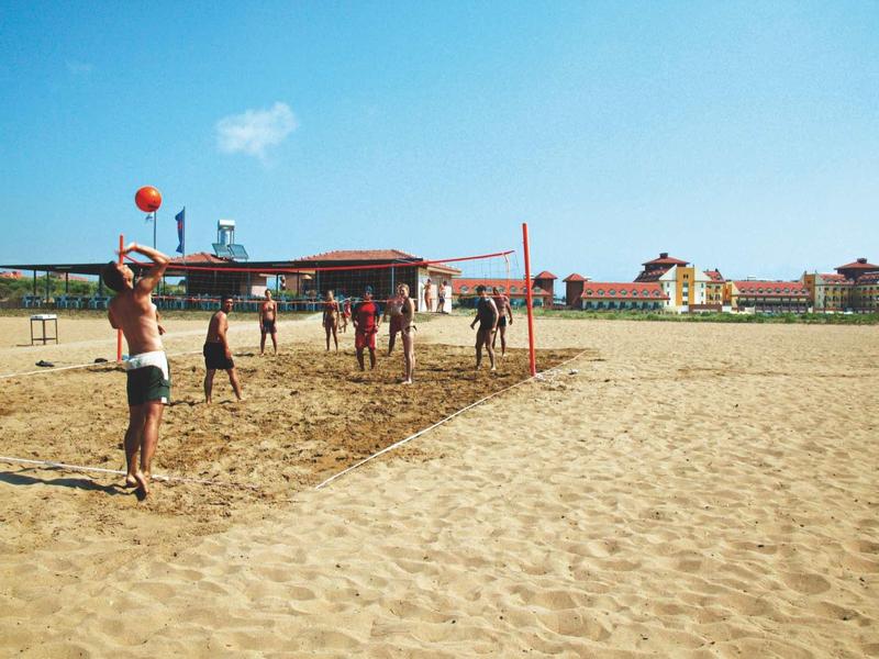 People playing volleyball on a sandy beach in front of a hotel building under clear sky.