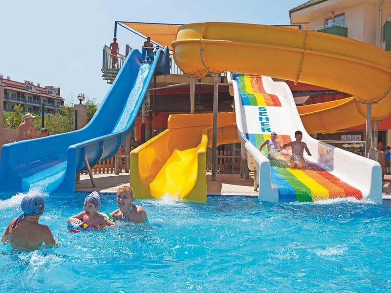 Colorful water slides and children playing in a hotel pool on a sunny day.