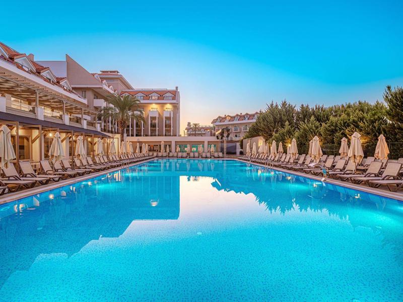 Groot hotelzwembad met ligstoelen en parasols onder een heldere hemel.