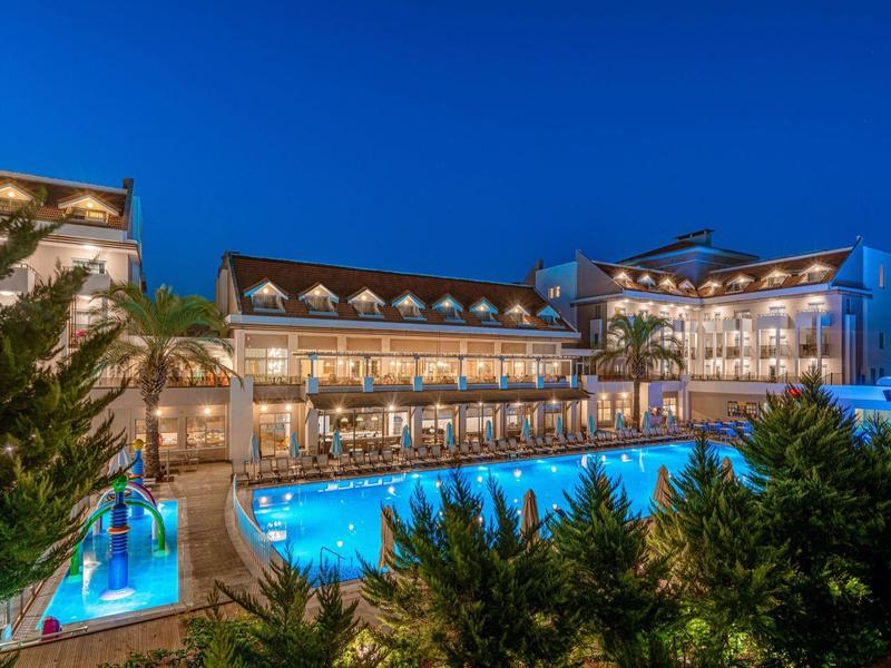 Verlicht hotel met groot zwembad 's nachts, omgeven door groen.