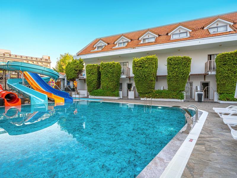 Hotelzwembad met glijbanen, ligstoelen en aangrenzend gebouw met plantenmuur.