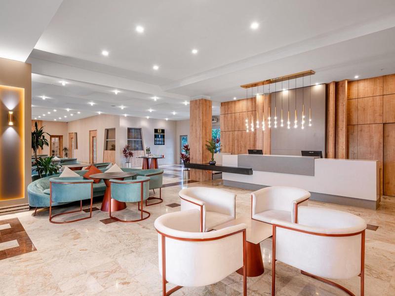 Lichte hotel lobby met moderne receptie, fauteuils en banken in warme tinten.