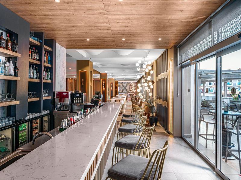 Moderne hotelbar met lange witte bar, houten bekleding en uitzicht op het buitenterras.