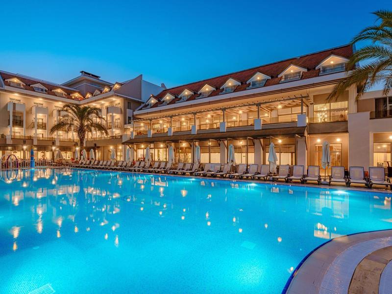Verlicht hotel met groot zwembad en palmentuin bij nacht.