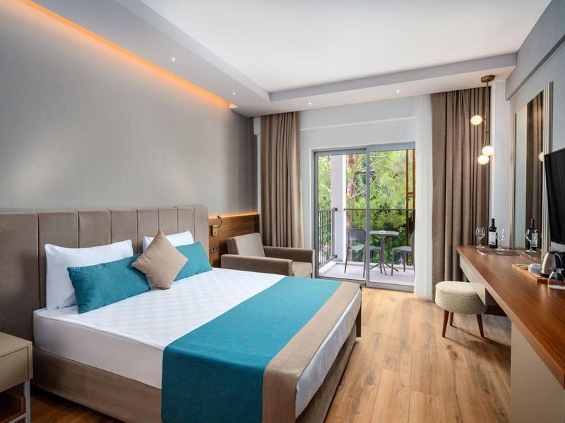 Modern hotelkamer met tweepersoonsbed, bureau en balkon met uitzicht op groen.