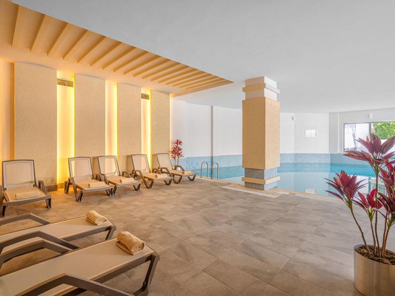 Overdekt zwembad met meerdere ligstoelen en warme verlichting naast grote ramen.