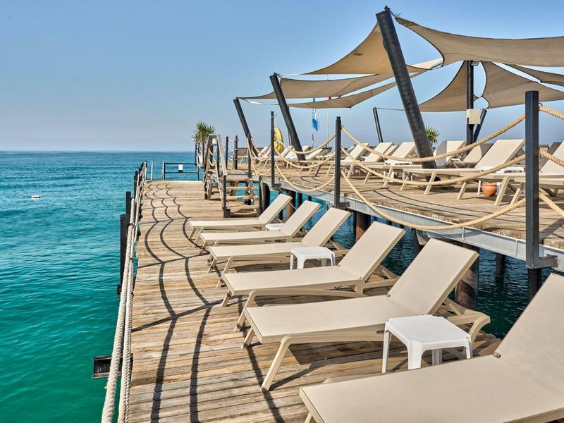 Terrasse ensoleillée au bord de la mer avec des chaises longues et des pare-soleil par une journée claire.