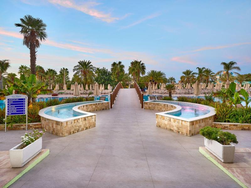 Vue d'un large chemin pavé avec deux bassins d'eau et des palmiers dans une station balnéaire.