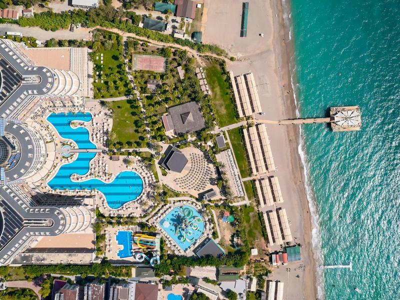 Vue aérienne d'un complexe avec plusieurs piscines à côté d'une plage de sable et d'une mer turquoise.
